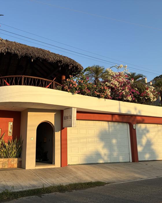 Hotel Bonito entrance from the scenic road: white walls with red trim, rooftop palapa and bougainvillea