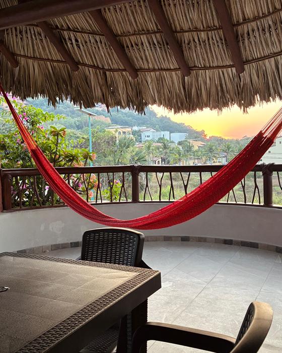 Red hammock under the palapa with a view of the hills